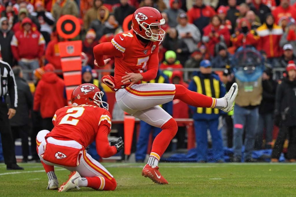 Kansas City Chiefs kicker Harrison Butker No 7 kicks field goal with teammate on green field Wallpaper