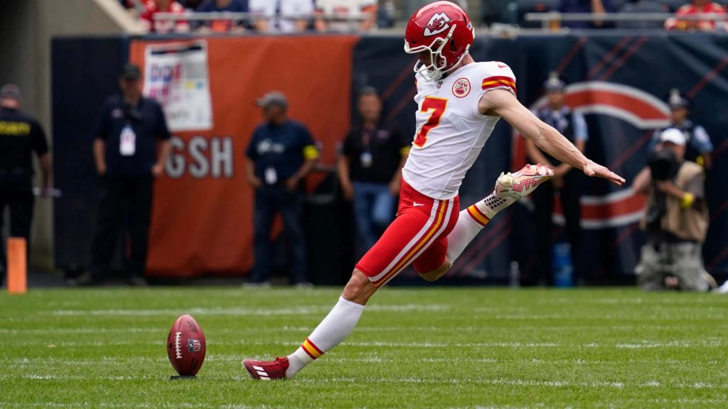 Kansas City Chiefs kicker Harrison Butker in white red uniform kicking field goal on stadium grass Wallpaper