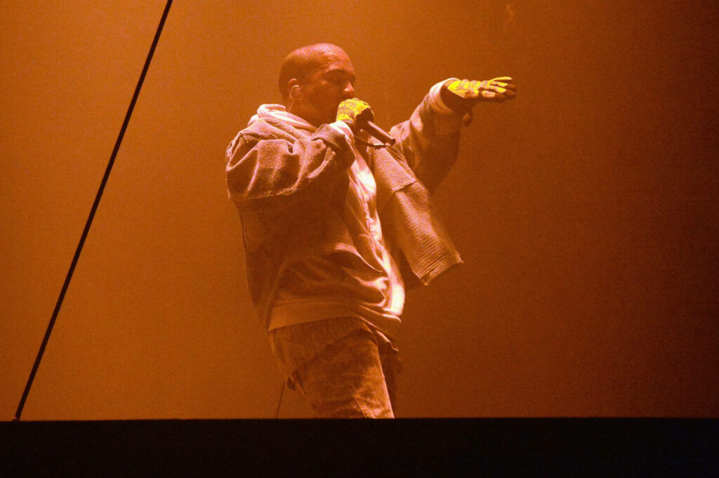 Kanye West: Dynamic Saint Pablo Stage Performance in Hazy Orange Wallpaper