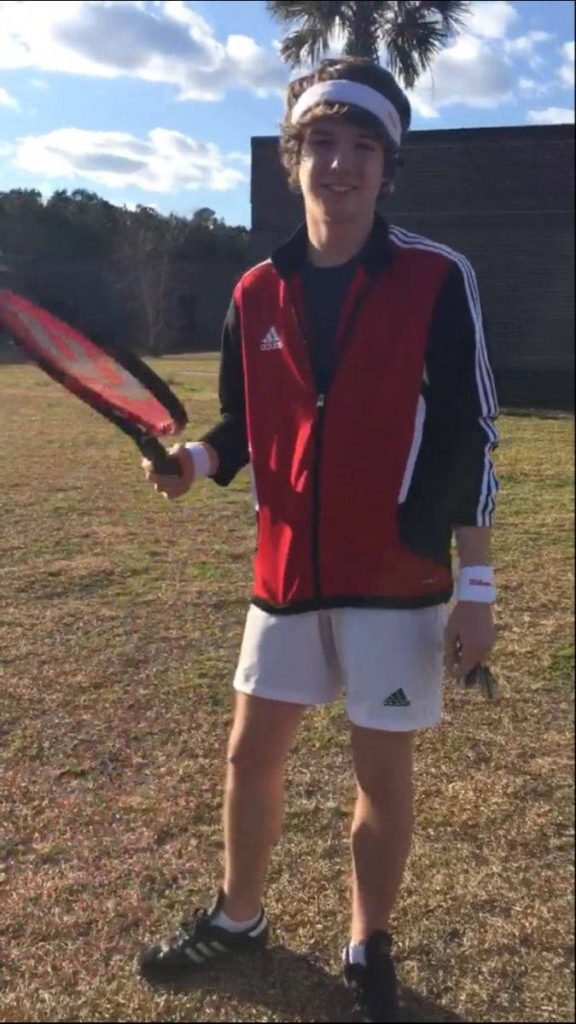 Karl Jacobs in red black track jacket white shorts holding tennis racket outdoor bright wallpaper
