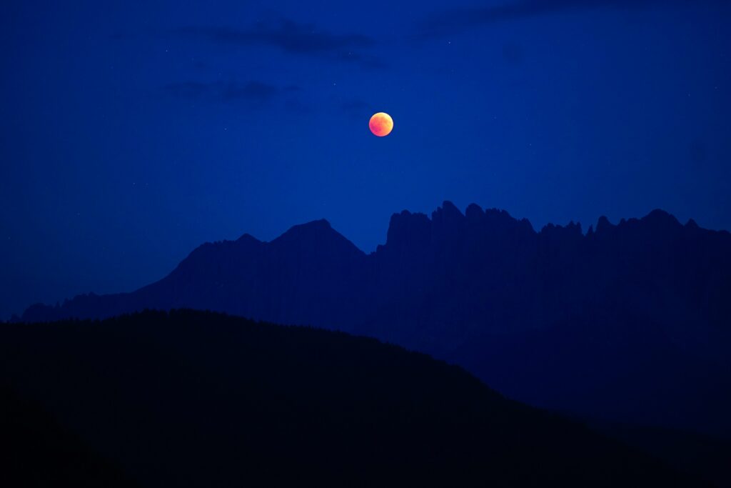 Karneid mountains Italy at night with full moon glowing over deep blue sky wallpaper background