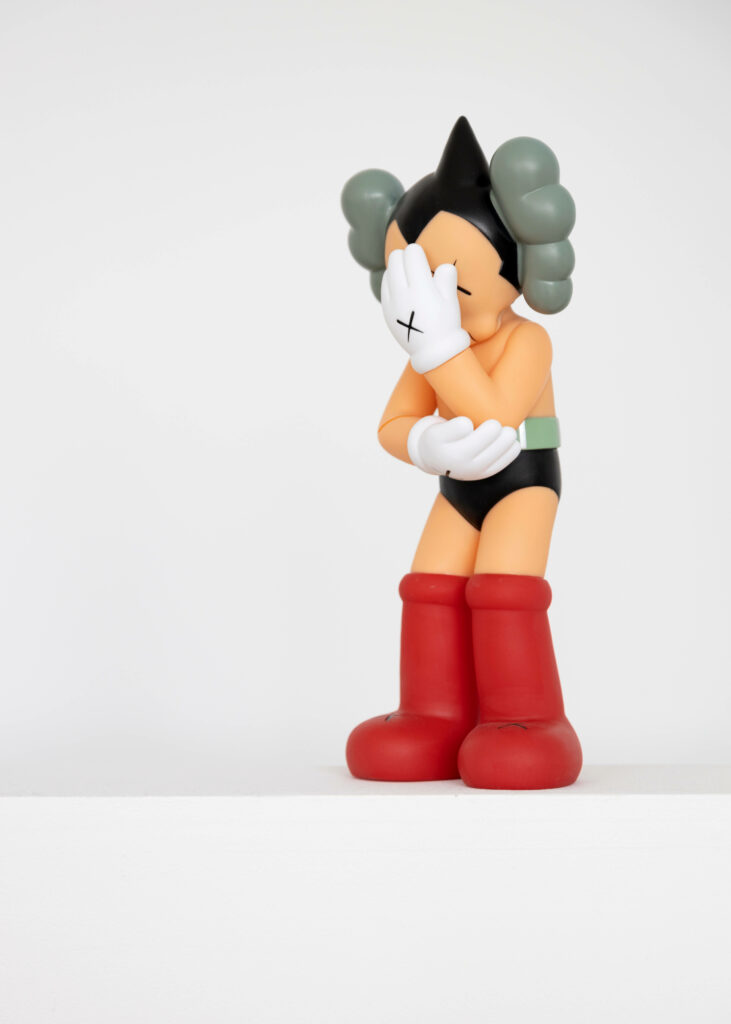 Kaws Astro Boy Edition figure wallpaper with crossed-out eyes and hands on white background