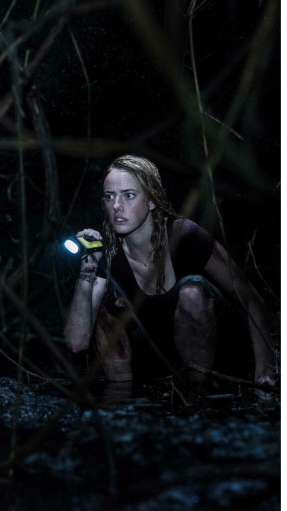 Kaya Scodelario crouching with flashlight in dark swamp intense wallpaper background