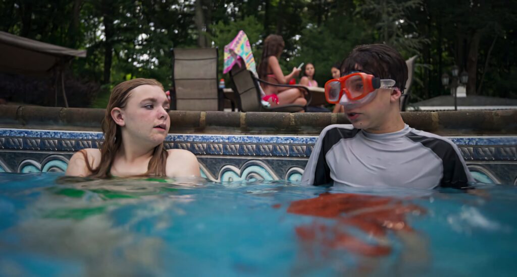 Kayla and Gabe from Eighth Grade in a backyard pool sharing an awkward moment at pool party Wallpaper