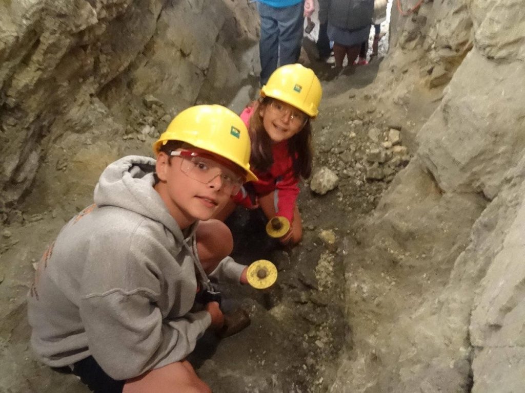 Two children in yellow hard hats explore narrow rocky tunnels at Hidee Gold Mine Colorado Wallpaper