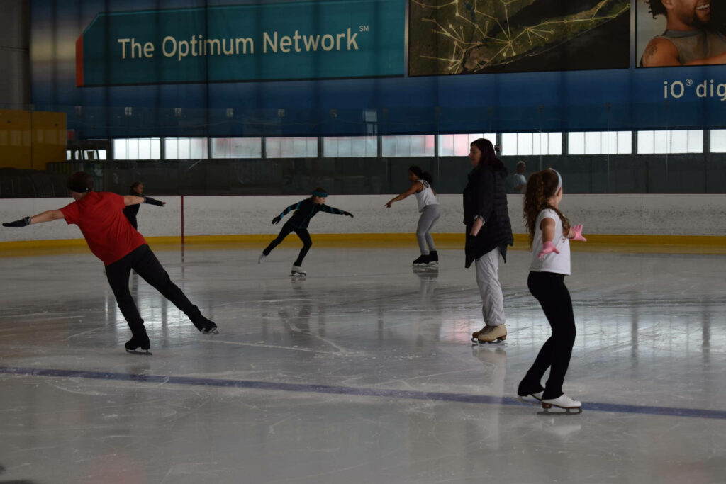 Kids practicing figure skating on indoor rink with instructor in fun energetic lesson setting Wallpaper