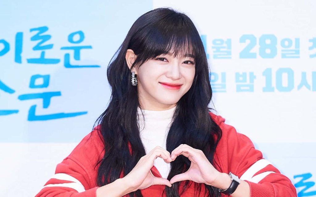 Kim Se-jeong in red jacket smiling and making heart gesture at press event wallpaper background