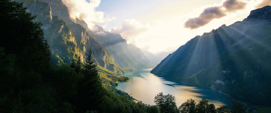 Golden sunrise over calm Klöntalersee glacial lake surrounded by lush Swiss alpine mountains Wallpaper