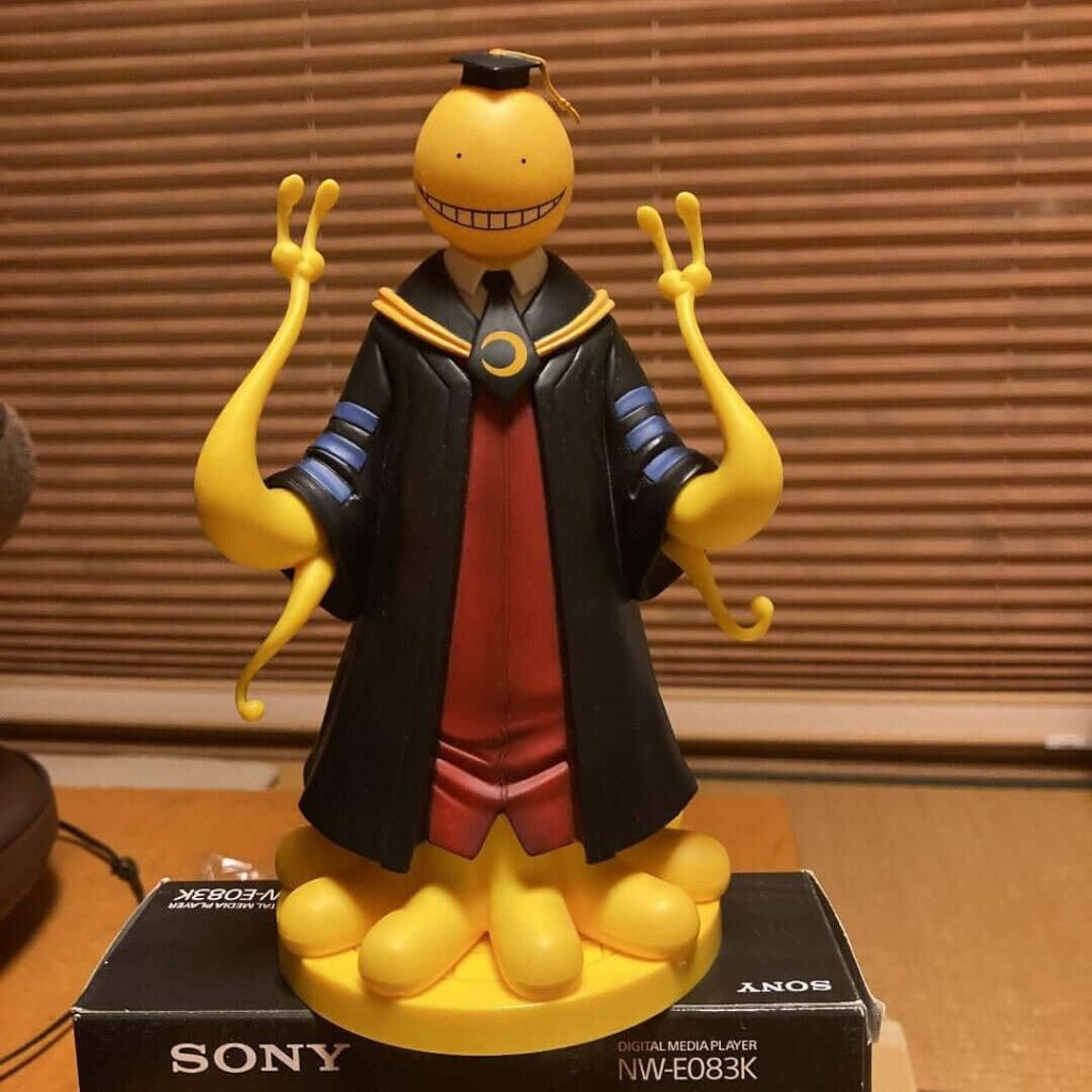 Koro-sensei figurine in graduation robe flashing peace sign on Sony digital player box background Wallpaper