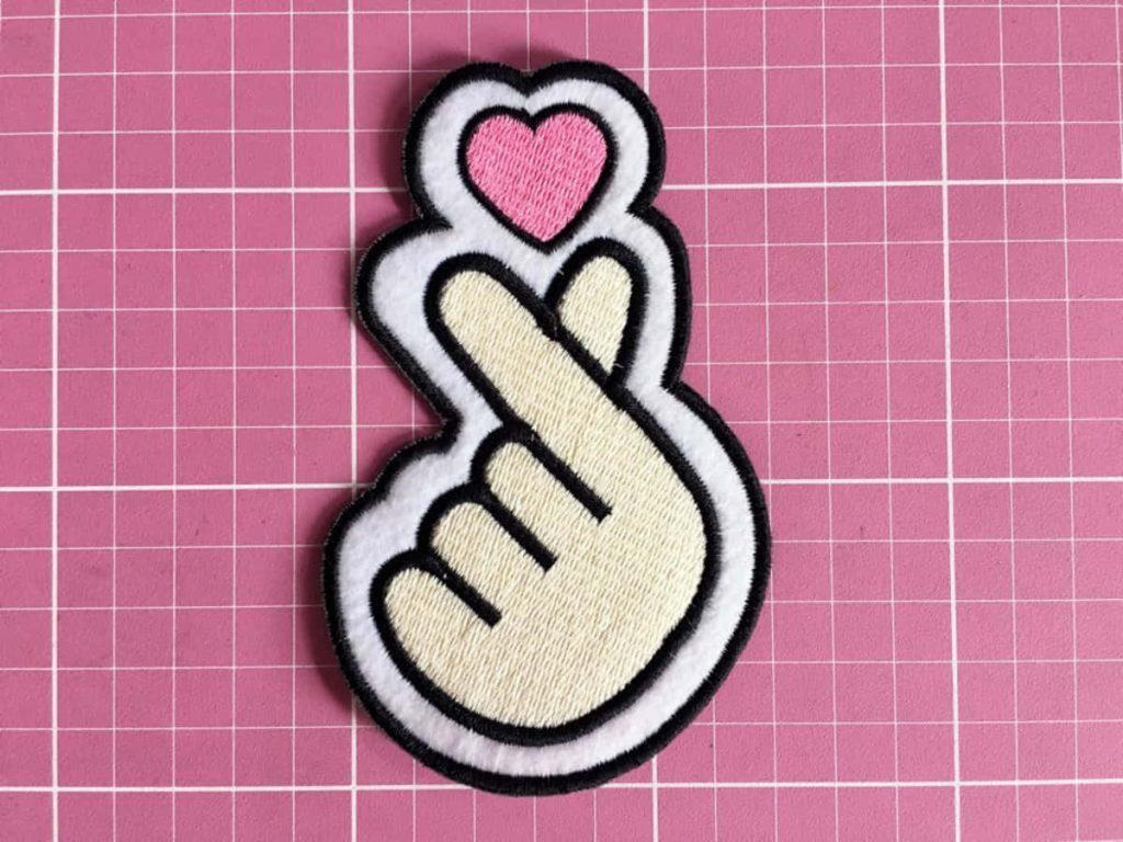 Embroidered K-pop finger heart patch cream hand pink heart on pink grid cutting mat background Wallpaper