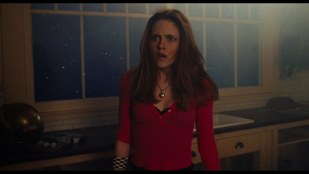 Kristen Stewart in a dramatic red outfit with intense expression in a modern kitchen setting Wallpaper