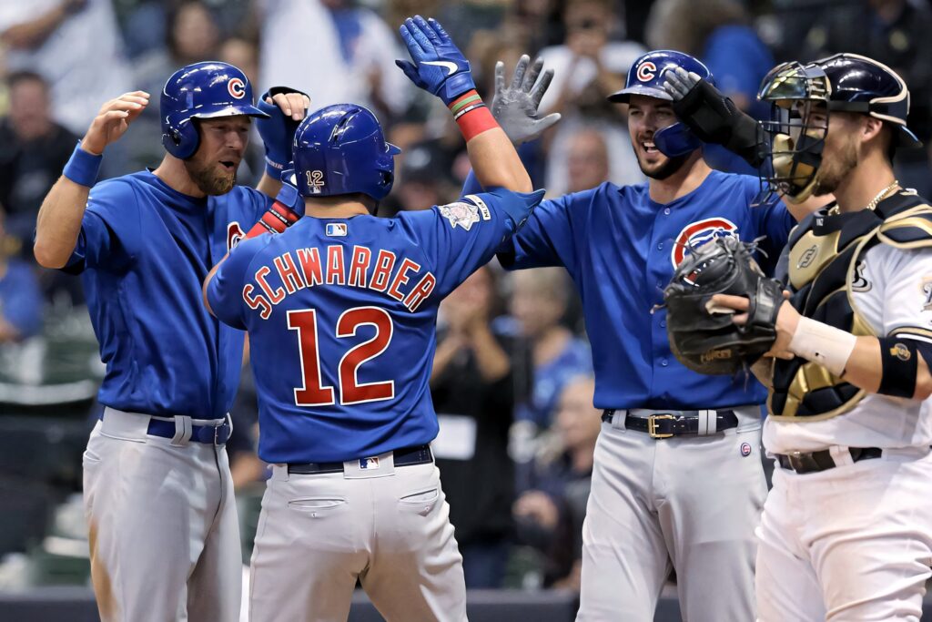 Kyle Schwarber and Chicago Cubs teammates high-five in blue uniforms celebrating on field Wallpaper