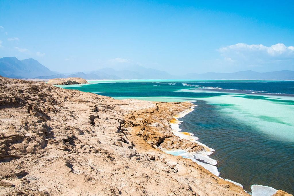 Vibrant turquoise Lake Assal Djibouti with rocky shore and mountains under clear blue sky wallpaper