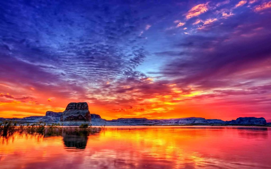 Lone Rock at Lake Powell sunset with vibrant orange and purple sky reflecting on calm water wallpaper