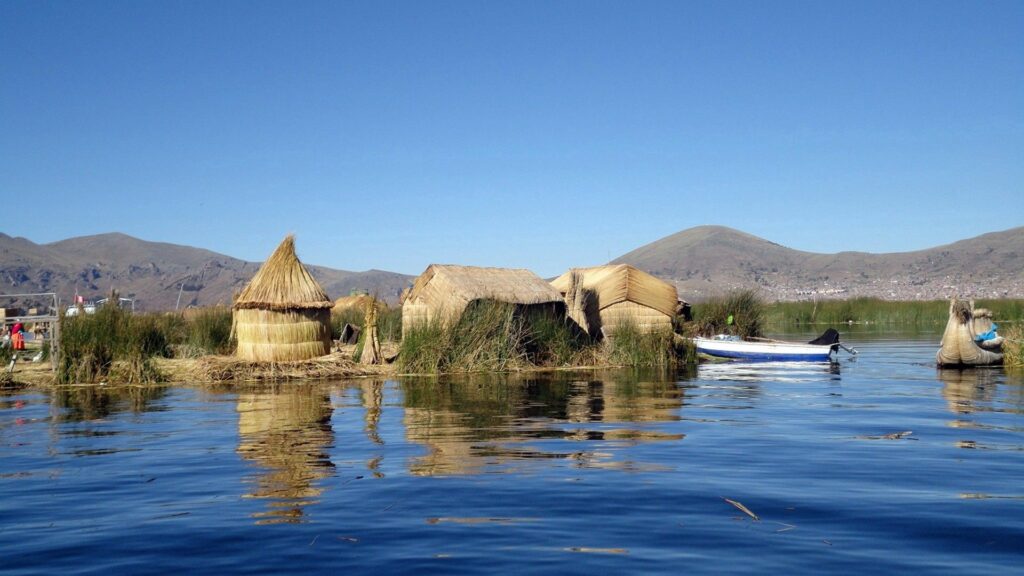 Lake Titicaca peaceful scene with reed huts boat reflective water green grass rolling hills Wallpaper