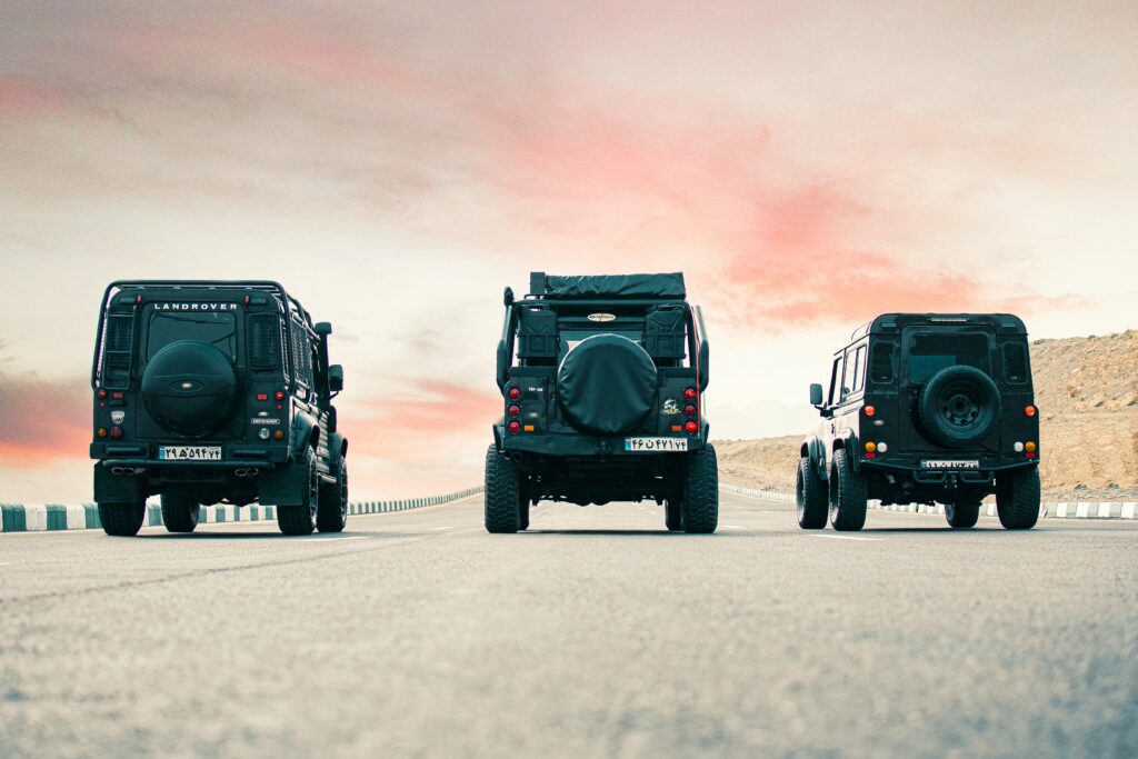 Three Rugged Land Rover Defenders on Scenic Road Wallpaper