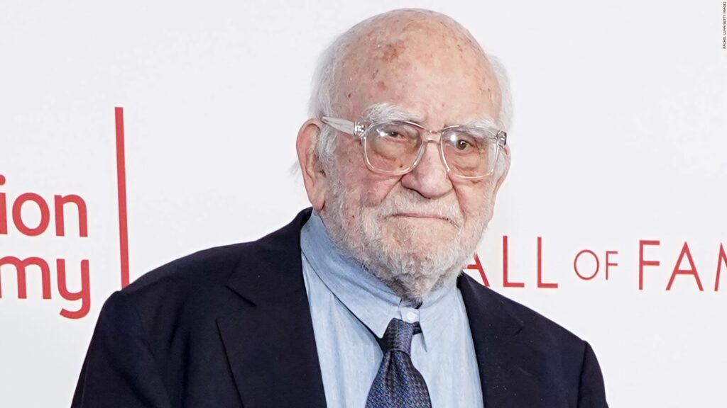 Ed Asner in classic navy suit blue shirt patterned tie at event white backdrop red signage Wallpaper