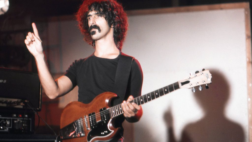 Vintage wallpaper of Frank Zappa playing electric guitar on stage with dramatic lighting shadows