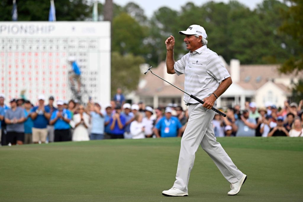 Legendary golfer Fred Couples smiling waving with putter on sunny golf course near leaderboard Wallpaper