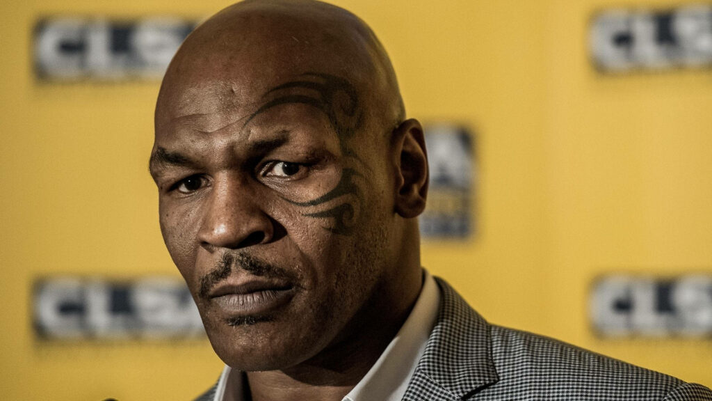 Iconic Ink: Mike Tyson's Legendary Face Tattoo in Gray Suit with Vibrant Yellow Blur Wallpaper