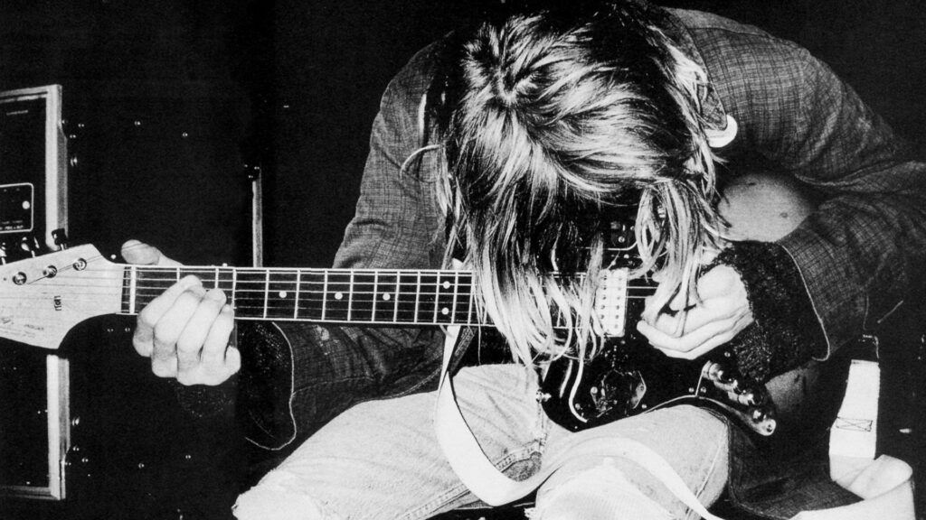 Nirvana's Guitar Guru: Captivating Wallpaper of Kurt Cobain, the Legendary Lead Vocalist, Engrossed in a Mesmerizing Guitar Solo