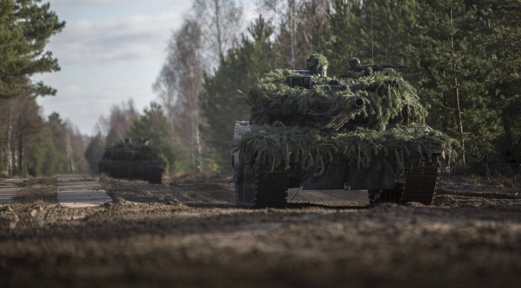 Leopard 2 tanks camouflaged with pine branches on muddy forest trail during military training Wallpaper