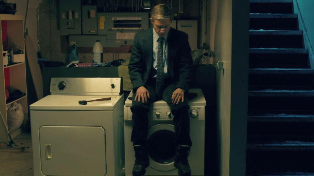 Lester Nygaard from Fargo seated on washing machine in dim basement moody tense wallpaper background