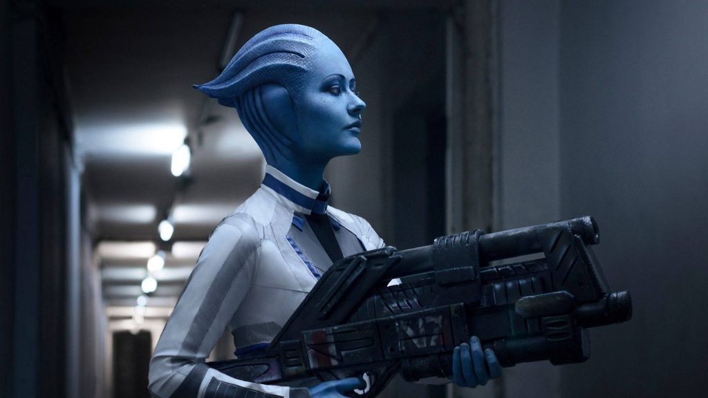 Liara T'Soni Mass Effect cosplay in futuristic corridor holding sci-fi rifle blue tones wallpaper