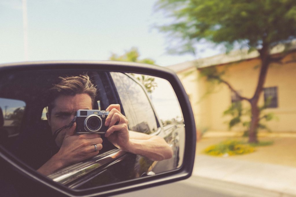Man holding vintage camera reflected in car side mirror warm natural light artistic 4k image Wallpaper