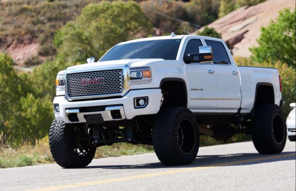 Lifted white GMC Sierra Denali HD with rugged tires on scenic road bright daylight truck wallpaper