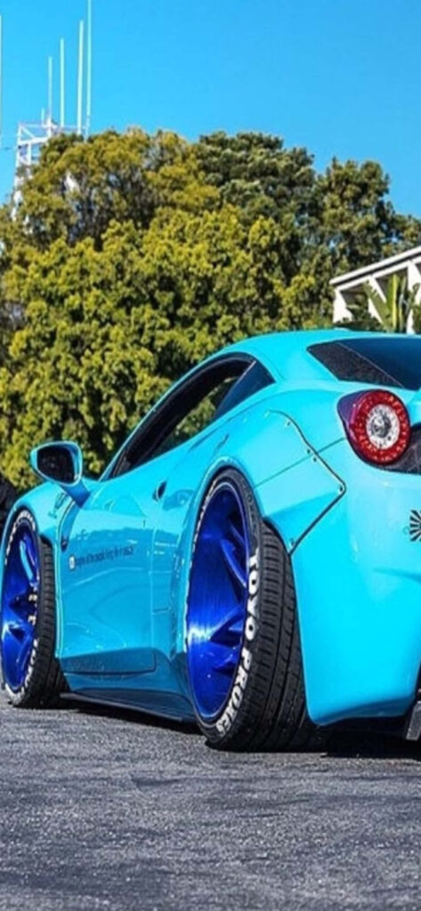 Light blue Ferrari 458 with custom blue rims parked outdoors by green trees and clear sky Wallpaper