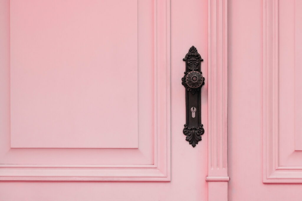 Ornate dark metal handle on soft pink paneled door vintage aesthetic wallpaper background