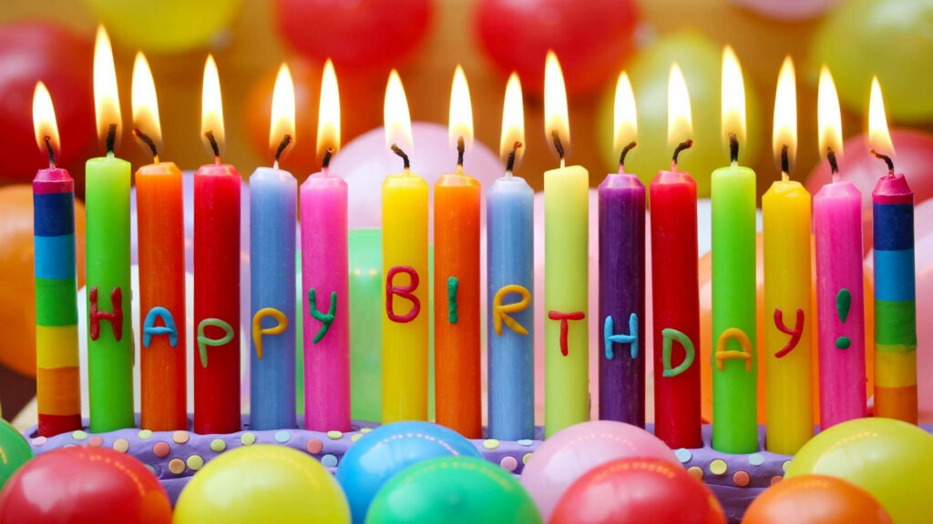 Vibrant birthday wallpaper with colorful lit candles spelling HAPPY BIRTHDAY and festive balloons