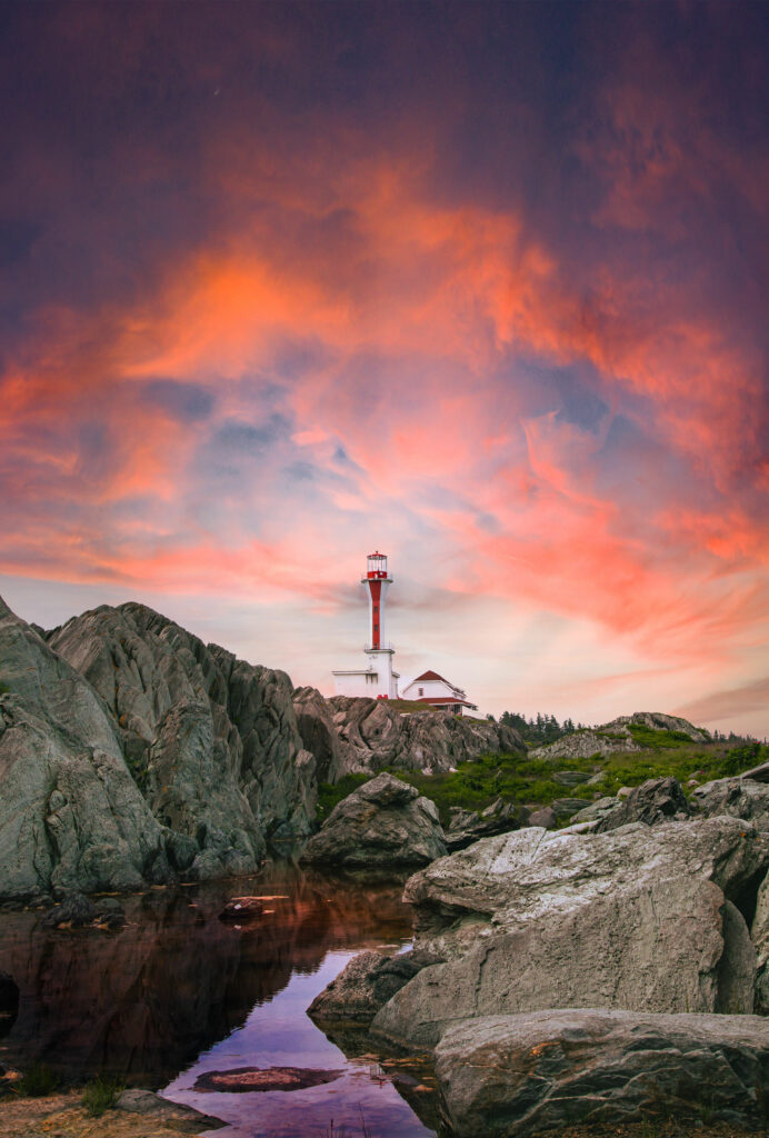 Lone lighthouse on rocky riverbank with vibrant sunset sky natural landscape wallpaper background