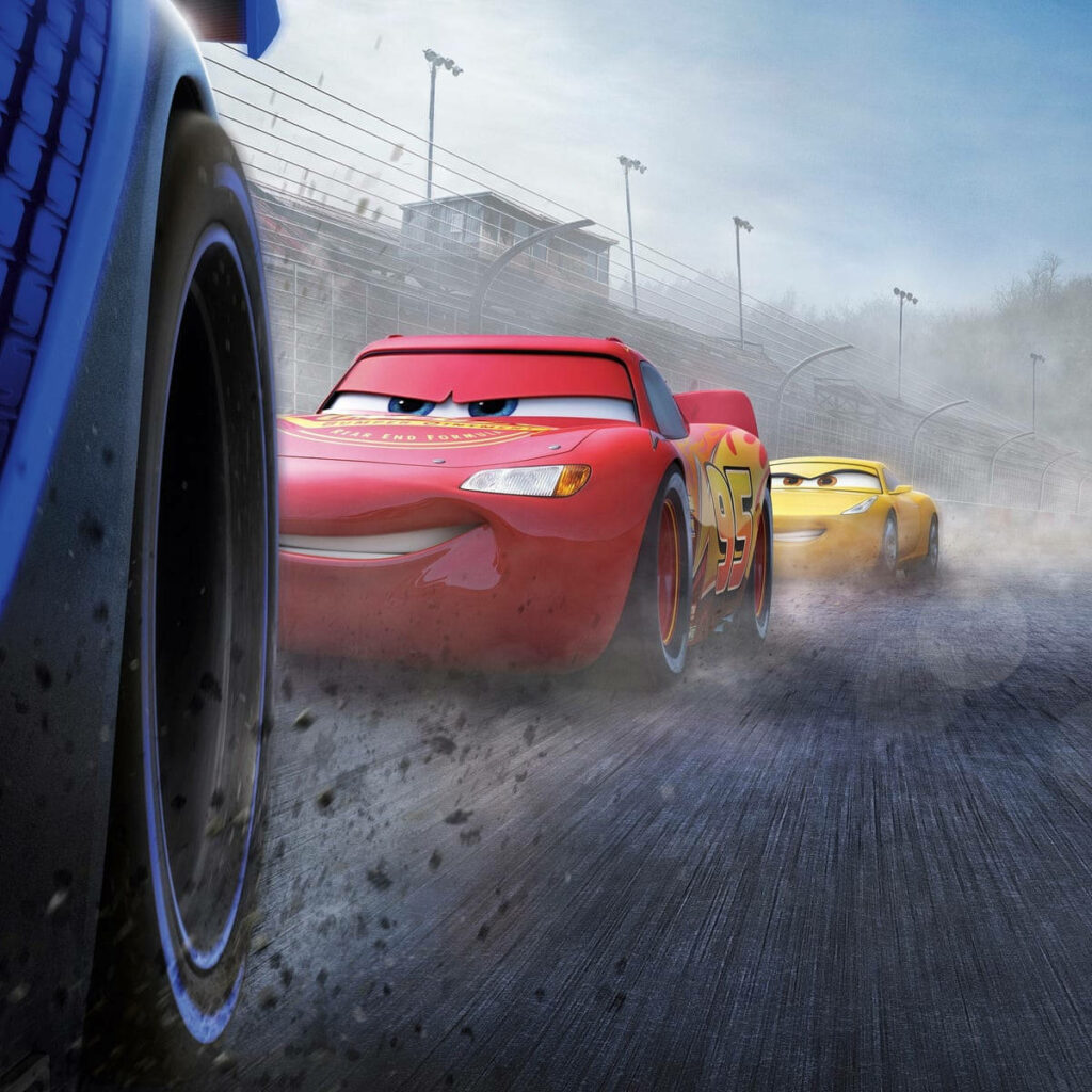 Lightning McQueen and Cruz Ramirez racing fast on vibrant Cars 3 racetrack with dynamic motion blur Wallpaper