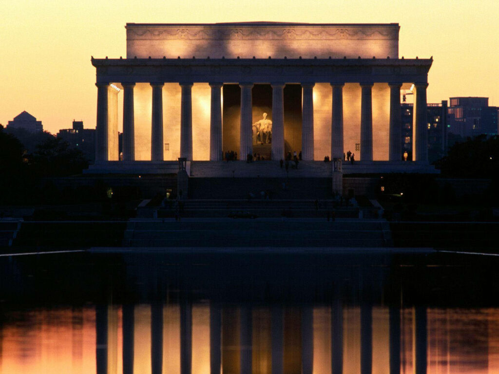 Lincoln Monument glowing at golden hour with reflections and warm sunset hues on water Wallpaper