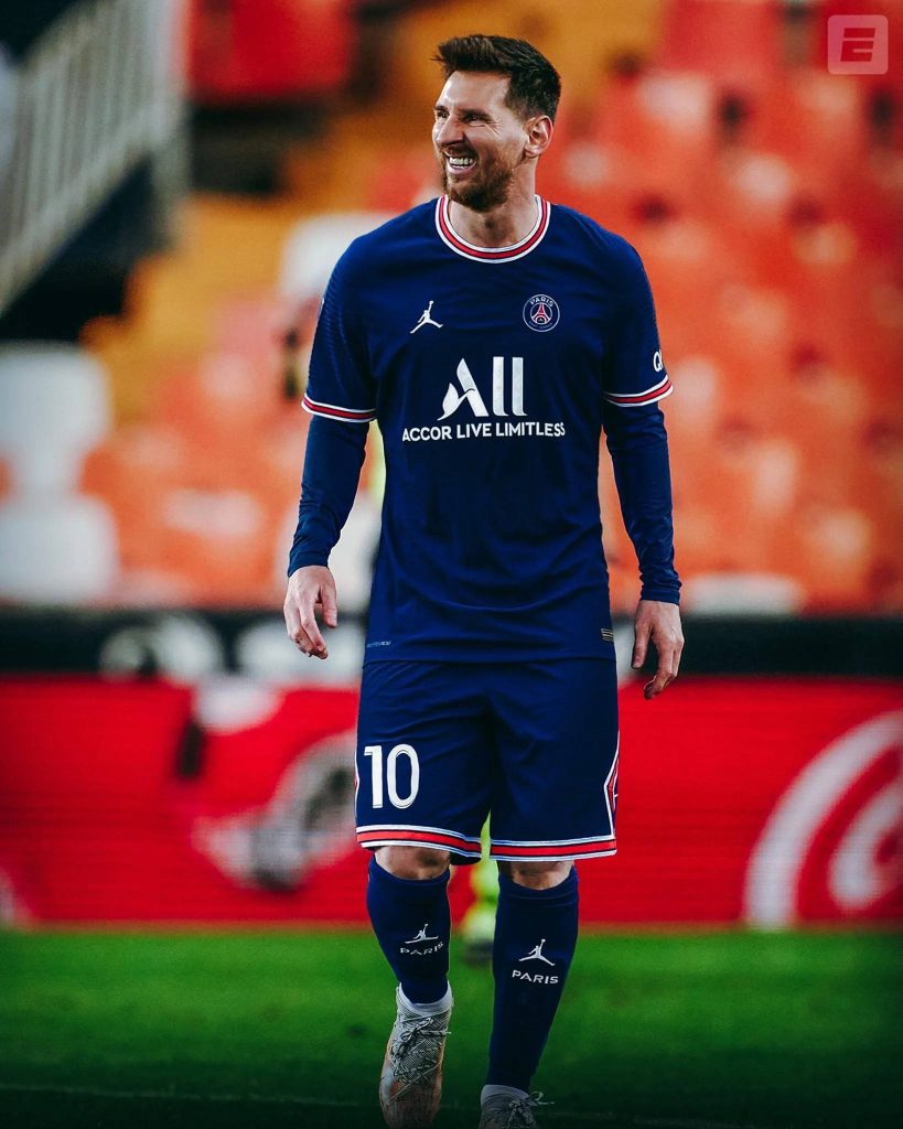 Lionel Messi smiling in navy Paris Saint-Germain kit with blurred stadium background wallpaper
