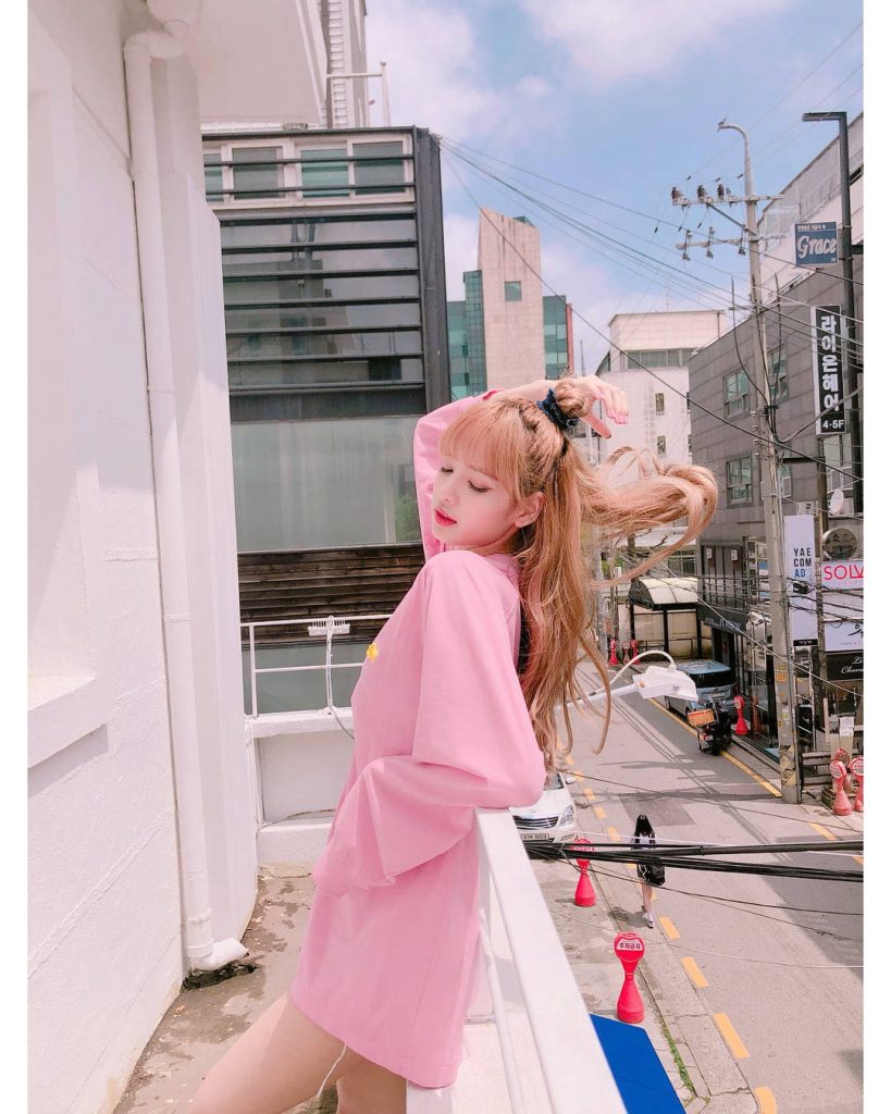 Lisa from BLACKPINK on sunny city balcony wearing pink long-sleeve vibrant urban wallpaper