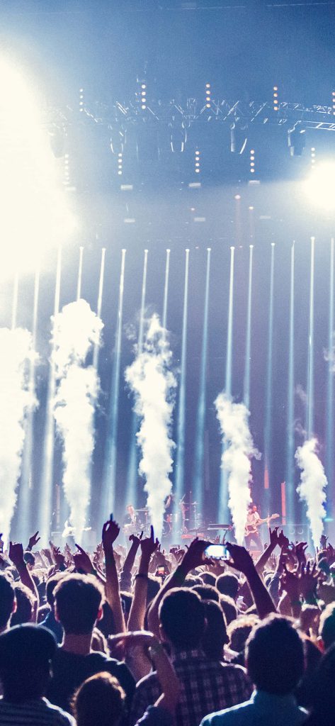 Crowd with raised hands enjoying live concert under blue lights and vertical smoke plumes wallpaper