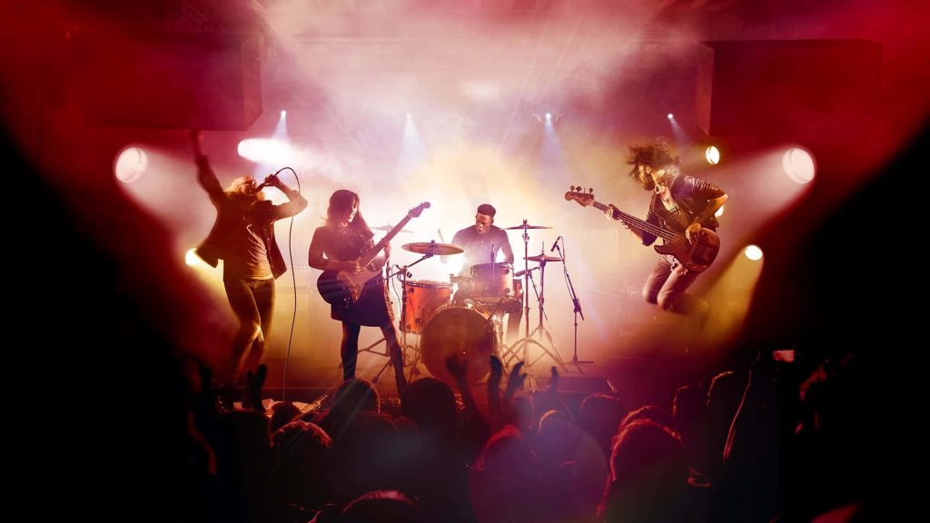 Live rock concert wallpaper with band on red lit stage and fans silhouetted in foreground