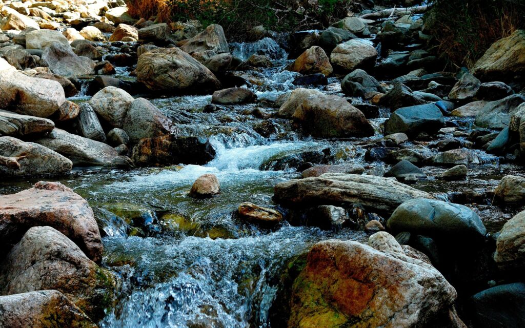 Lively mountain river flowing over smooth stones with vibrant blues greens and browns nature wallpaper