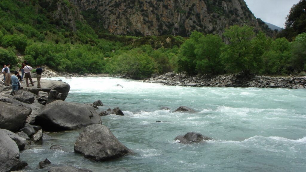 Lively river with strong current over stones by green trees and mountains tourists enjoy outdoors Wallpaper
