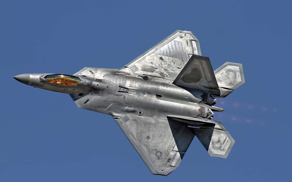 Lockheed Martin F-22 Raptor fighter jet in mid-flight with sleek design and afterburner glow Wallpaper