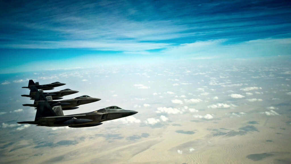 Lockheed Martin F-22 Raptor fighter jets soaring in formation above landscape under blue sky Wallpaper