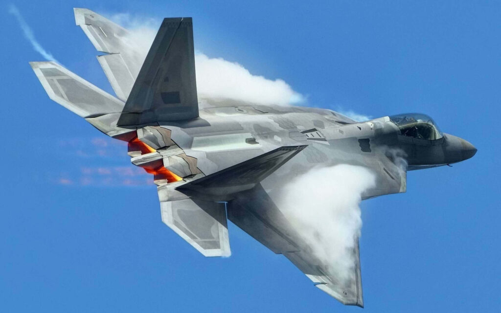 Lockheed Martin F-22 Raptor jet in flight with glowing afterburners and vapor trails against blue sky Wallpaper