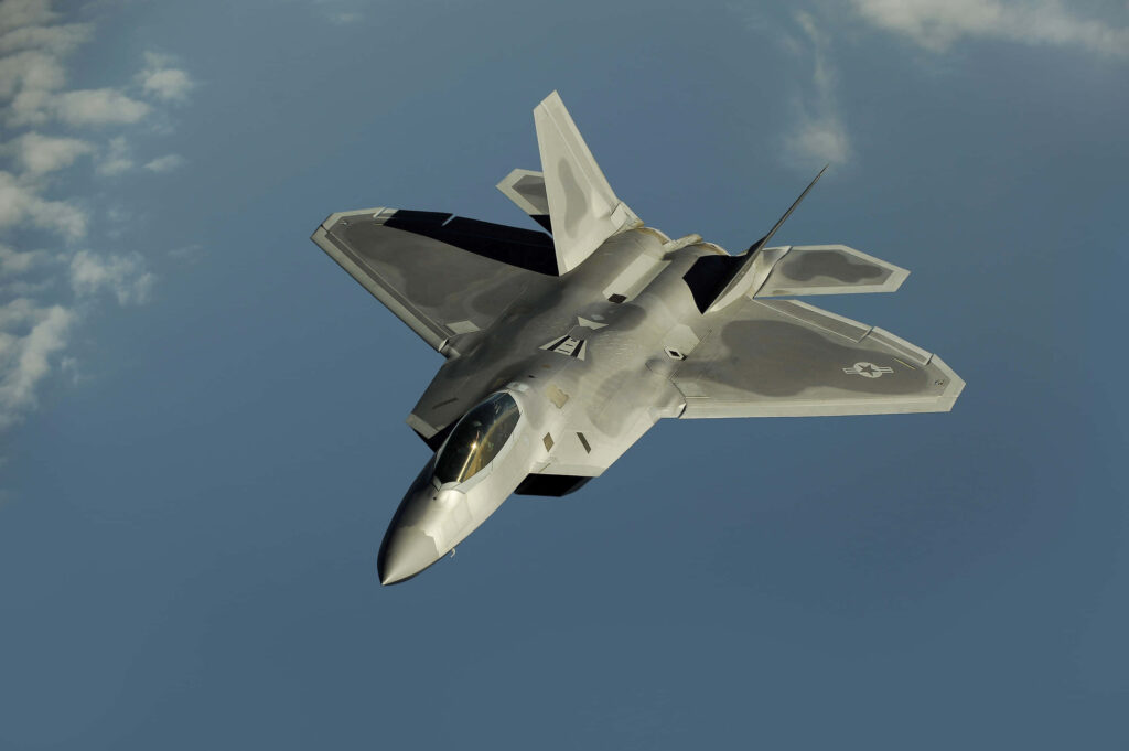 Lockheed Martin F-22 Raptor jet in flight with matte gray stealth design and soft cloud background Wallpaper