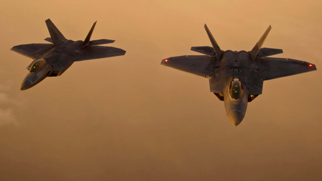 Two Lockheed Martin F-22 Raptor jets soaring at dusk with golden sky showcasing stealth design Wallpaper