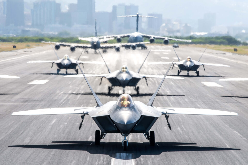 Fleet of Lockheed Martin F-22 Raptor jets taxiing on runway with blurred city skyline background Wallpaper