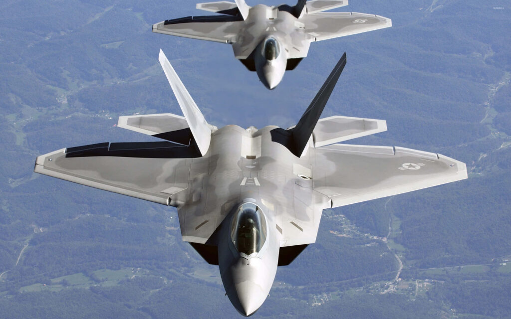 Two Lockheed Martin F-22 Raptor fighter jets flying in formation over forested landscape wallpaper