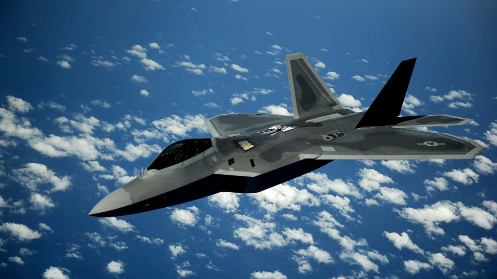 Lockheed Martin F-22 Raptor stealth fighter jet soaring above blue sky with scattered clouds Wallpaper